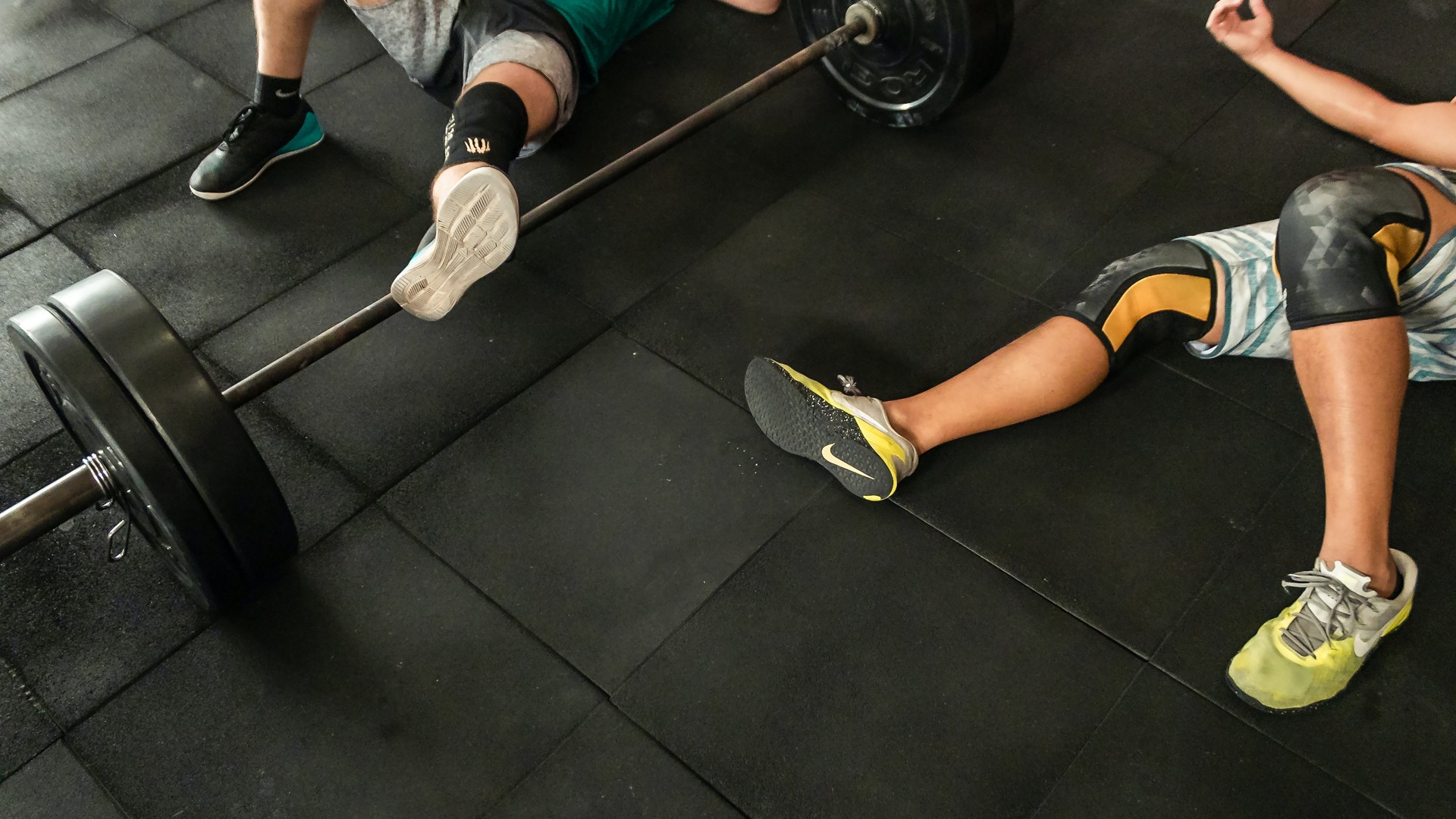 Two male athletes on gym floor after workout next to barbell