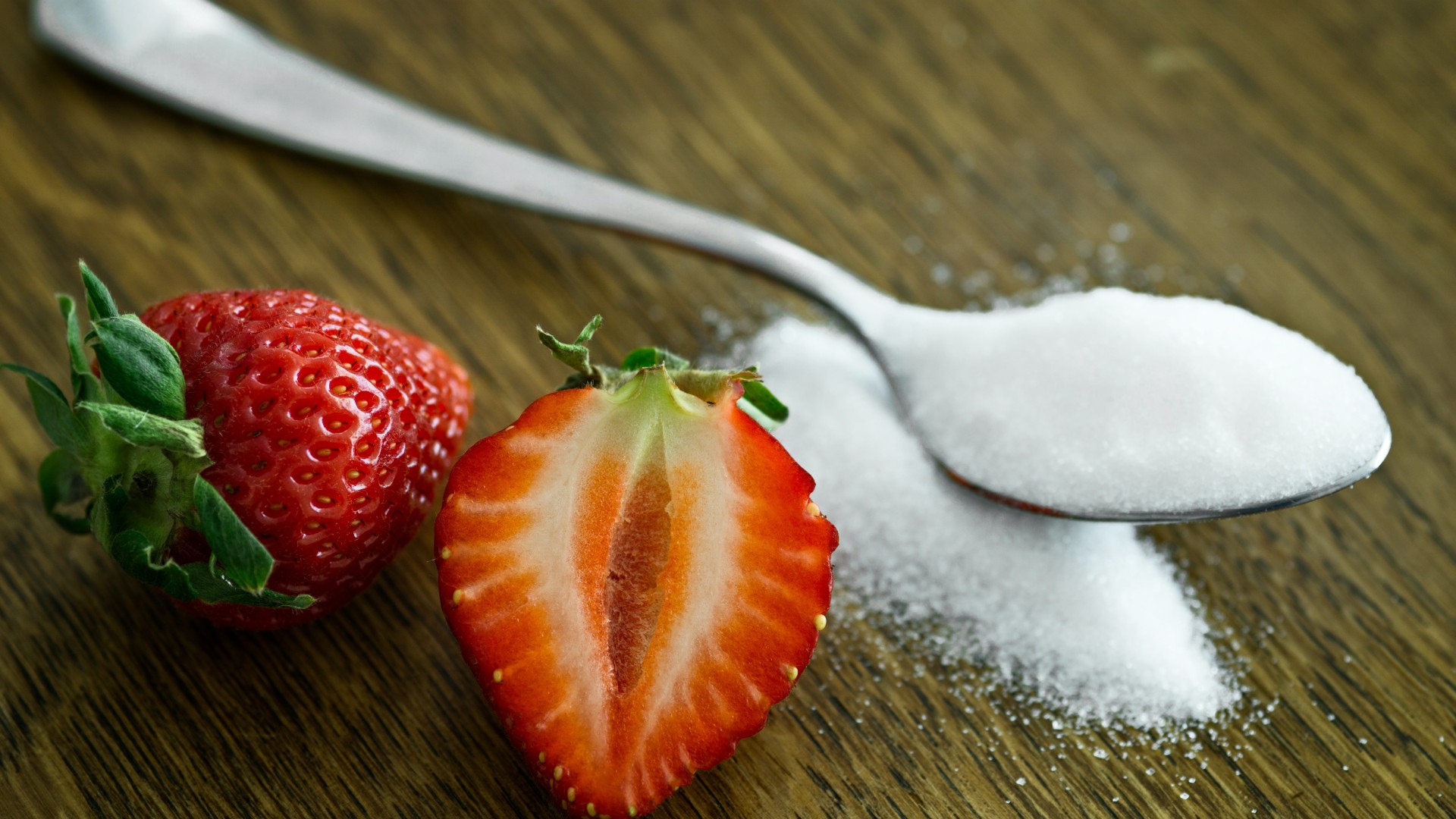 Teaspoon of sugar with strawberries on table